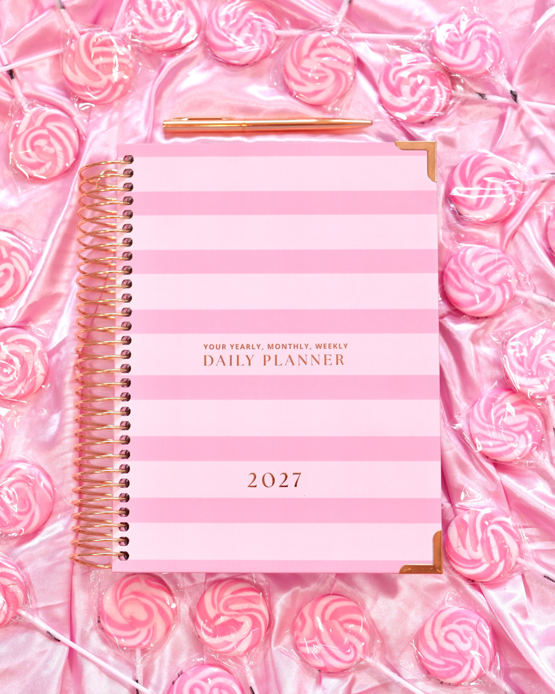 Pink striped 2027 Daily Spiral Planner with gold spiral binding among pink swirl candies