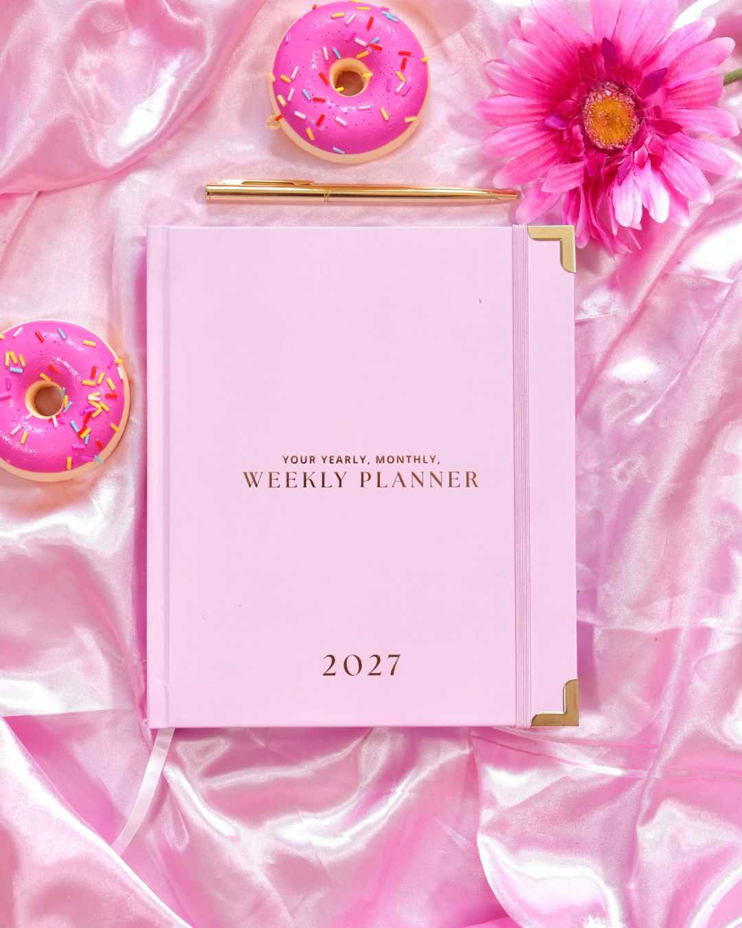 Pink 2027 Weekly Mini Planner with gold corners beside a gold pen, pink donuts, and a pink flower