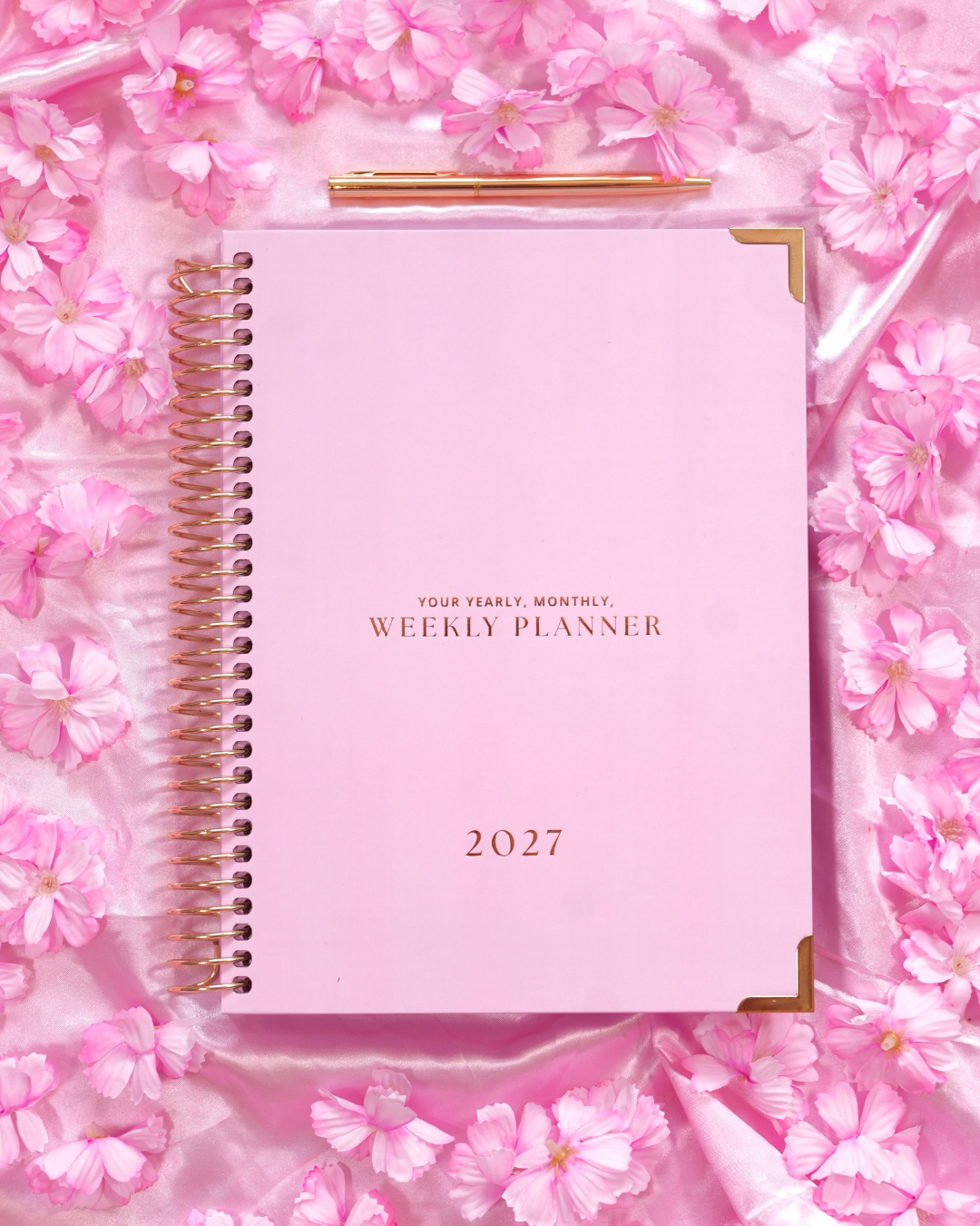 Pink 2027 Weekly Spiral Planner with gold spiral binding among pink blossoms