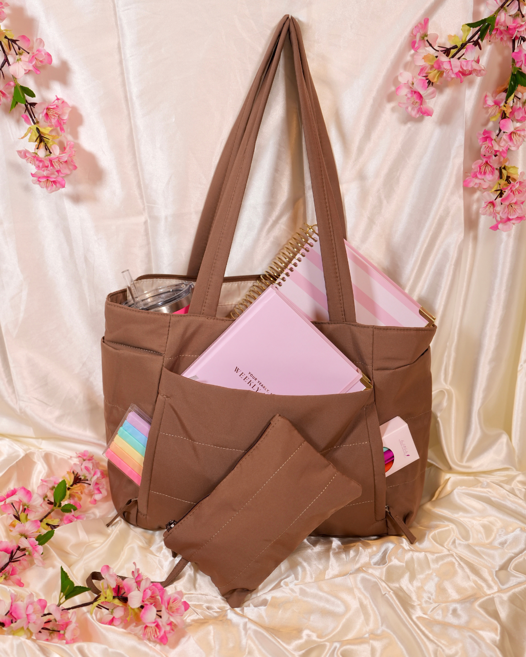 Brown Travel Tote holding a planner, a tumbler, and a pouch on cream satin