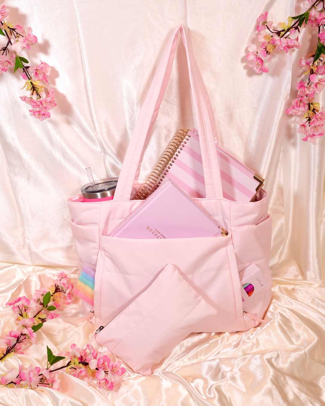 Pink Travel Tote holding a planner, a tumbler, and a pouch on cream satin
